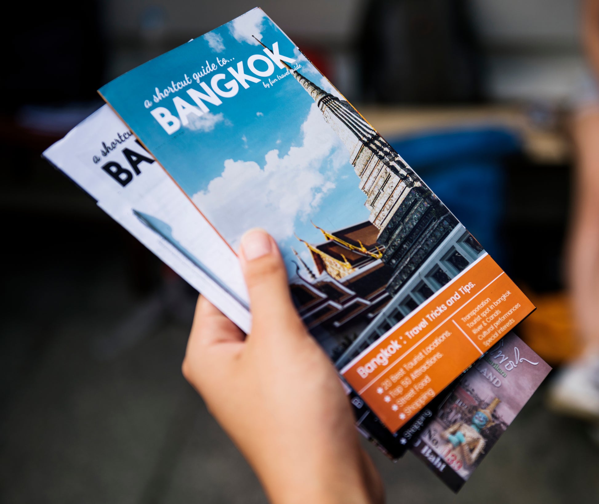Hand holding a brochure titled 'A Shorter Guide to Bangkok' with a blurred background.