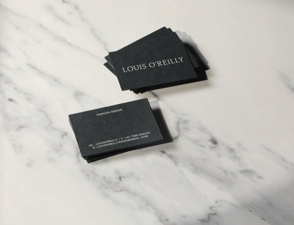 Black business cards with 'Louis O'Reilly' on a marble surface