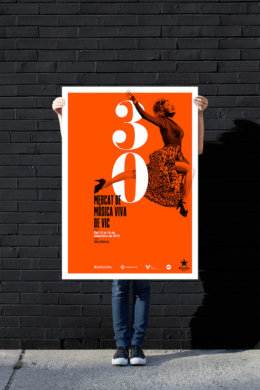 Person holding an orange poster with white text against a black brick wall.