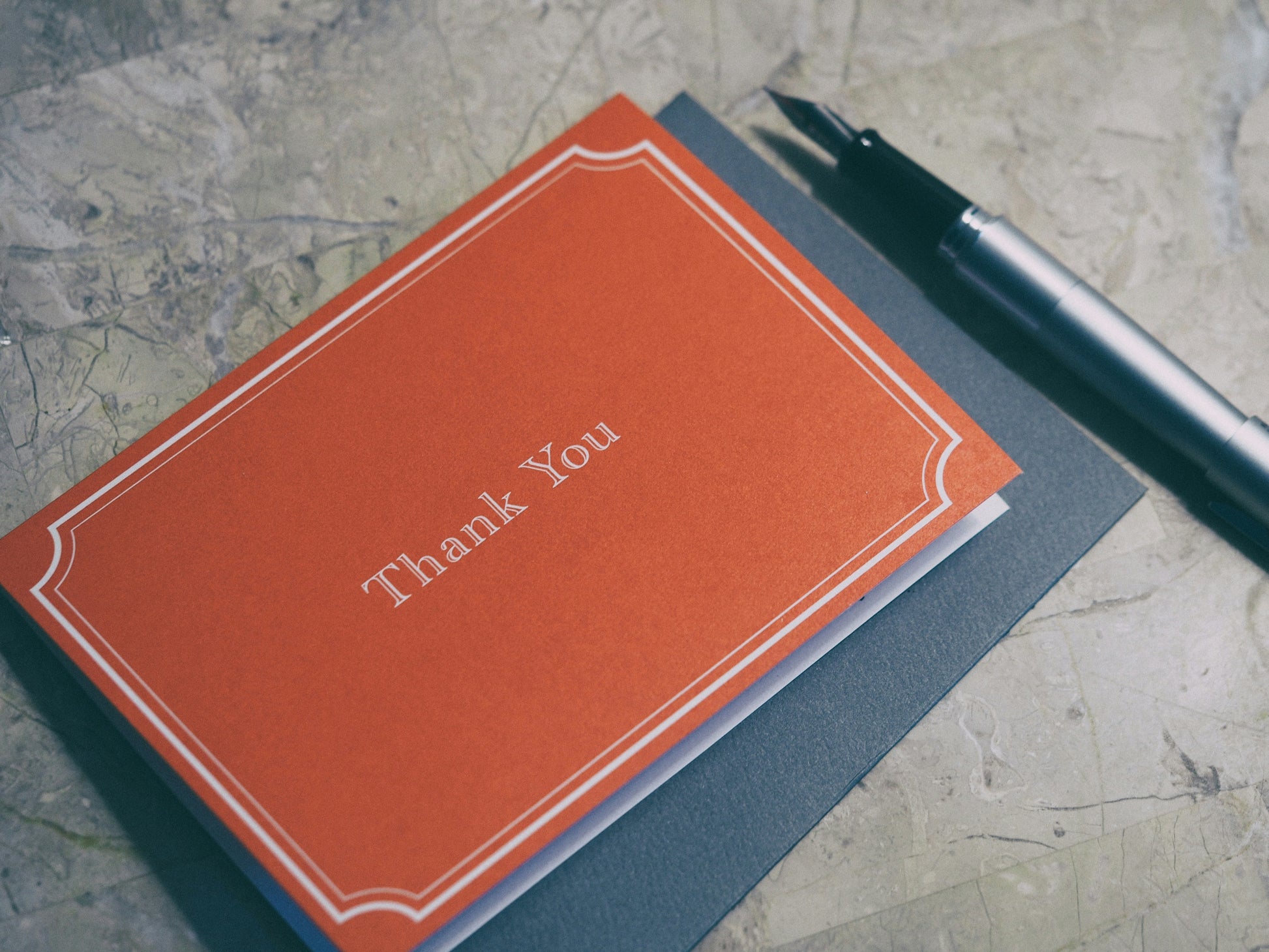Orange 'Thank You' card on a textured surface with a pen.