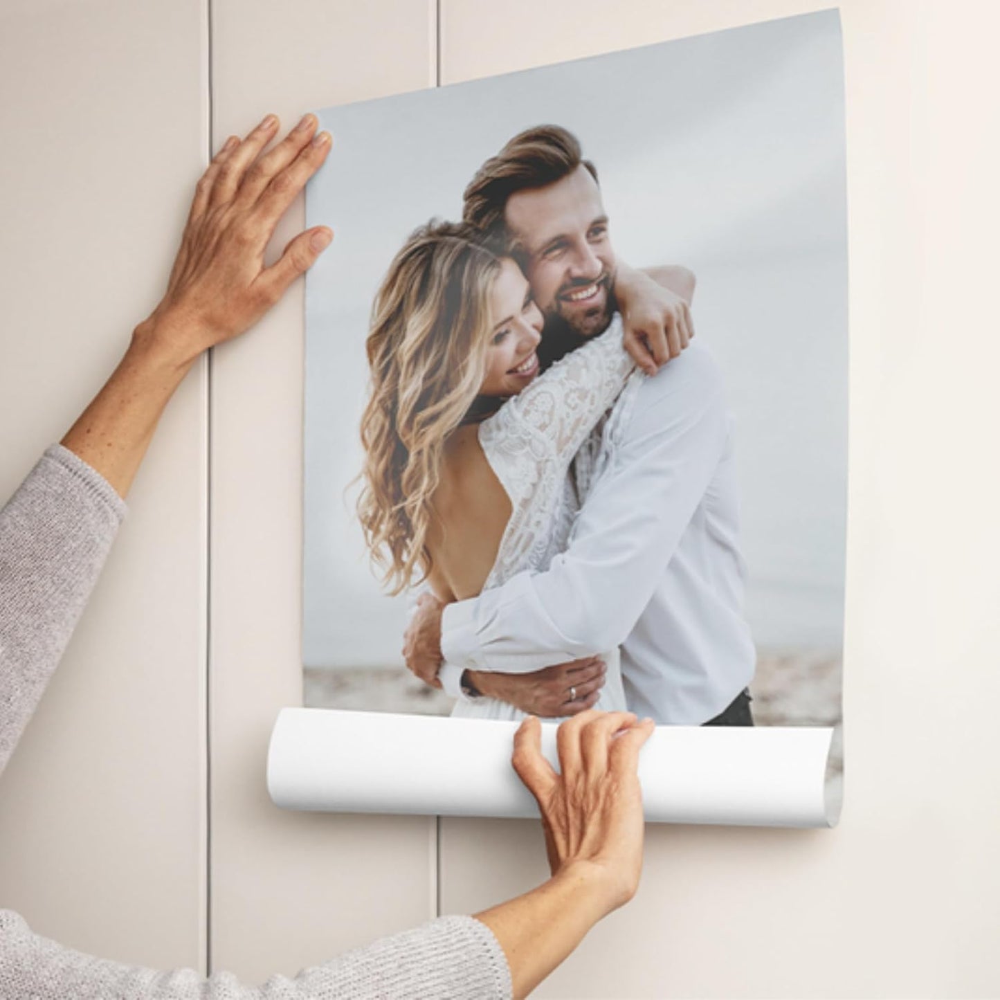 Person unrolling a photo of a couple from a roll on a light-colored wall.